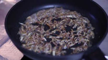 Bir adam kendi mutfağında pişirirken pastırma tavada kızartılıyor.