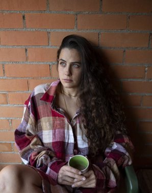 Elinde kahve fincanı tutan, kafasını çeviren, tuğladan duvara yansıyan bir kadın.