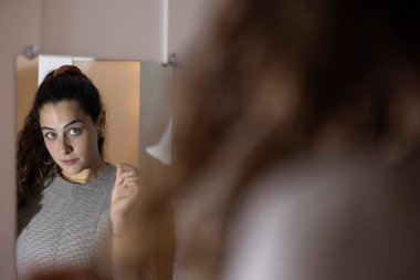 Bir kadın aynadaki yansımasına bakıyor. Kimliğini ve öz imajını düşünüyor.