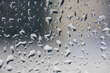 Cama düşen su damlalarının yakın görüntüsü yumuşak yansımalar ve bulanık şekillerle soyut bir zemin oluşturuyor. Yağmuru, nemi ve hava kavramlarını temsil eden minimum ve modern doku.