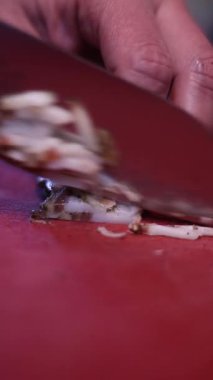 Kırmızı kesme tahtasındaki eti kesmek için bıçak kullanan bir şefin elleri.