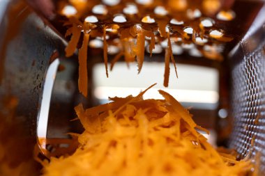 Taze rendelenmiş havuçlar metal bir rendeleyicinin içindeki yığının üzerine düşüyor.