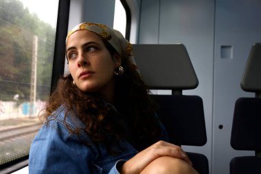 Trenle seyahat ederken manzarayı düşünen genç bir kadın.