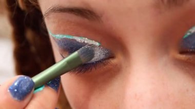 Makyaj sanatçılarının elinin bir kadının göz kapağına mavi göz farı sürmesi aşırı yakın plan.