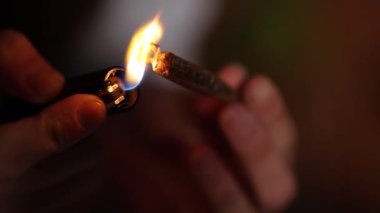 Erkek ellerinin karanlık bir ortamda el yapımı esrar sigarasını yaktığı yakın çekim görüntüsü