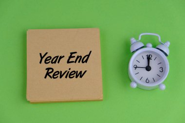 Alarm saati, kalem ve Yıl Sonu İncelemesi ile yeşil arkaplan üzerine yazılmış notların seçici odak noktası.