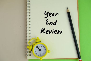 Alarm saati, kalem ve Yıl Sonu İncelemesi ile yeşil arkaplan üzerine yazılmış notların seçici odak noktası.