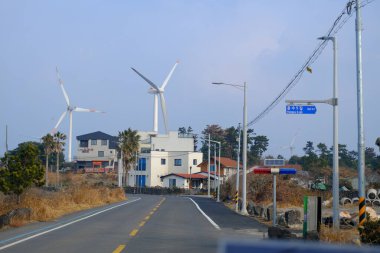 Jeju, Güney Kore - 11 Şubat 2026: Gün batımındaki Jeju cazibesi. Kıyıya yakın beton kuleler yel değirmeni