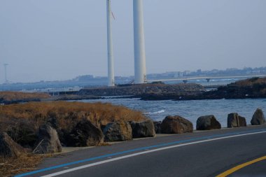 Jeju, Güney Kore - 11 Şubat 2026: Gün batımındaki Jeju cazibesi. Kıyıya yakın beton kuleler yel değirmeni