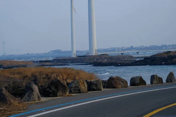Jeju, Güney Kore - 11 Şubat 2026: Gün batımındaki Jeju cazibesi. Kıyıya yakın beton kuleler yel değirmeni