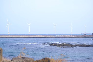 Jeju, Güney Kore - 11 Şubat 2026: Gün batımındaki Jeju cazibesi. Kıyıya yakın beton kuleler yel değirmeni