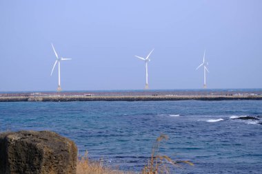 Jeju, Güney Kore - 11 Şubat 2026: Gün batımındaki Jeju cazibesi. Kıyıya yakın beton kuleler yel değirmeni