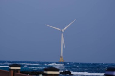 Jeju, Güney Kore - 11 Şubat 2026: Gün batımındaki Jeju cazibesi. Kıyıya yakın beton kuleler yel değirmeni