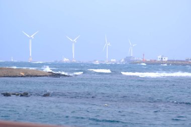 Jeju, Güney Kore - 11 Şubat 2026: Gün batımındaki Jeju cazibesi. Kıyıya yakın beton kuleler yel değirmeni