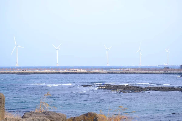 Jeju, Güney Kore - 11 Şubat 2026: Gün batımındaki Jeju cazibesi. Kıyıya yakın beton kuleler yel değirmeni