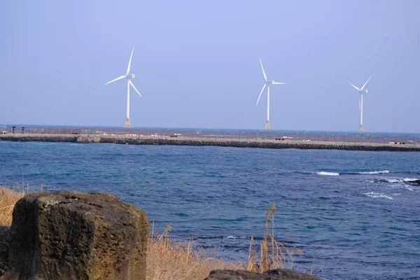 Jeju, Güney Kore - 11 Şubat 2026: Gün batımındaki Jeju cazibesi. Kıyıya yakın beton kuleler yel değirmeni