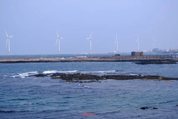 Jeju, Güney Kore - 11 Şubat 2026: Gün batımındaki Jeju cazibesi. Kıyıya yakın beton kuleler yel değirmeni