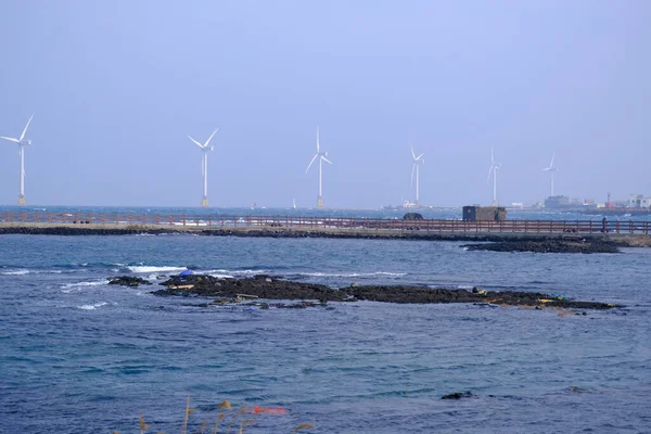 Jeju, Güney Kore - 11 Şubat 2026: Gün batımındaki Jeju cazibesi. Kıyıya yakın beton kuleler yel değirmeni