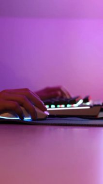 Pembe LED ışıklandırmada bilgisayar klavyesinde ve farede çalan ellerin yakın plan görüntüsü