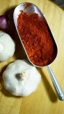 Taze sarımsak soğanları ve ahşap tahtanın yanına yerleştirilmiş kırmızı biber tozuyla dolu metal kepçenin en alt görüntüsü.