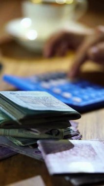 Mali yatırım ve bütçe planlaması için arka planda hesap makinesi olan tahtadan bir masanın üzerinde kağıt para banknotlarını sayarak erkeklerin ellerini kapat.