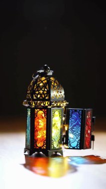 İslami bayram dekorasyonu için ahşap yüzeye canlı gölgeler bırakan renkli renkli Arap fenerinin kapı manzarası.