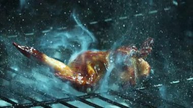 A single cooked chicken wing sits on a dark metal grill grate while being sprayed with water causing mist and steam to rise upward now