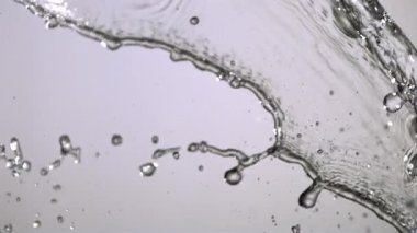 Kristal berrak su yavaş çekimde açık gri bir zemine doğru akar ve tüm çerçeve boyunca dinamik sıvı şekiller ve güzel damlacıklar yaratır.