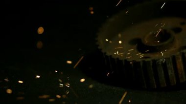 Paslı metal endüstriyel dişliler karanlık bir yüzeyde otururken, parlak turuncu kıvılcımlar şu anda görünmeyen bir öğütme ya da kaynak işleminden geçiyor.