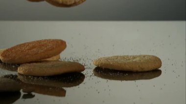 Yuvarlak kahverengi şekerli kurabiyeler düşer ve koyu bir yansıtıcı yüzeyin üzerine yığılırken ince kırıntılar ve granüller şimdi lezzetli tatlı şekerlerin etrafında zıplıyorlar.