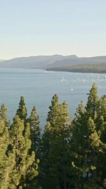 Yüksek açılı hava görüntüsü, yüksek yeşil çam ağaçlarının üzerinden yavaşça inerek, sıcak ve yumuşak güneş ışığıyla yıkanmış bir dağ manzarasına yuva yapmış çok sayıda tekne ve tekne rıhtımının bulunduğu sakin bir gölü ortaya çıkarıyor..