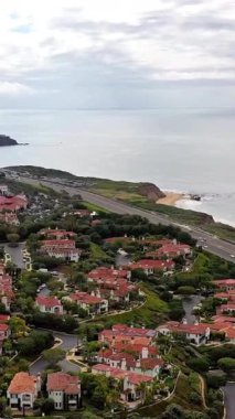 Okyanus dalgaları ve lüks uçurum kenarındaki evler arasında uzanan kıyı şeridinin hava manzarası bulutlu gökyüzünün altında manzaralı kıyı manzarasını gösteriyor.