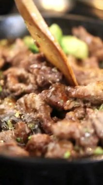 Biftek şeritleri ve brokoli çiçeklerinin ahşap spatulayla karıştırılarak tavada kızartılması ve lezzetli kahverengi sosla karıştırılması.