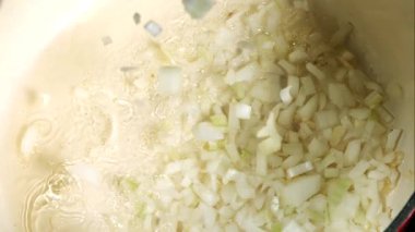 Doğranmış beyaz soğanlar yukarıdan sıcak yağ içeren büyük bir tencereye atılır. Soğanlar cızırdıyor ve kabarcıklar yüzeye yüksek açıyla vuruyor. Yakın çekim..