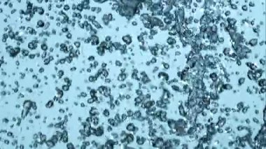 Ağır yağmur damlacıkları yavaş çekim yüksek hız yakalama ile açık mavi bir arkaplan önünde düşey olarak düşüyor ve sıçrıyor