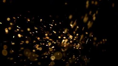 Parlak altın kıvılcımlar ve parlayan ateş parçacıkları yavaş çekimde zifiri karanlık bir zemine doğru uçuyor ve zıplıyorlar.
