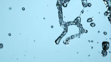 Suyun sıçramasını kapat ve çok güzel kristal damlacıklar oluştur. Yavaş çekimde, stüdyo ışıklarında parlak mavi bir arka plana karşı.