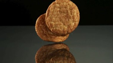 Altın kahverengi kurabiyeler yavaş çekimde siyah yansıtıcı bir yüzeye düşüyorlar ve bir stüdyo çekiminde koyu bir arkaplana karşı yığılıyorlar.