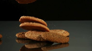 Taze pişmiş yulaf ezmeli kurabiyeler siyah arka plan stüdyosuna karşı karanlık bir yansıtıcı masaya düşüp üst üste yığılıyorlar.