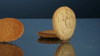 Koyu mavi bir stüdyonun arka planına karşı yavaş çekimde mavi bir yansıtıcı yüzeyin üzerine düşen çıtır çıtır kahverengi şekerli kurabiyeler.