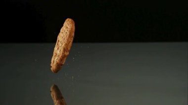 İki lezzetli yulaf ezmeli kurabiye düşüyordu ve yansıtıcı karanlık bir zeminde ağır çekimde yemek için katı siyah bir zemine karşı istifleniyordu.