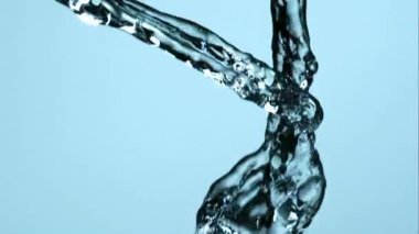 Kristal berrak su akıntıları havada çakışıyor ve hafifçe mavi arkaplana çarpıyor. Yavaş çekimde sıvı hareket ve saflığı gösteriyor.