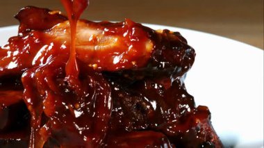 Kalın kırmızı barbekü sosu sulu ızgara domuz kaburgalarının üzerine dökülüyor.