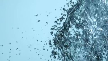 Suyun yoğun dikey duvarı sağ üst köşeden yavaş çekimde açık mavi arkaplana çarpıyor ve düşüyor.