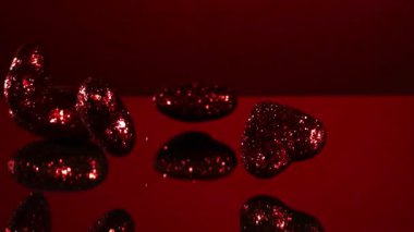 Pek çok kırmızı parıltılı kalp, sevgililer günü ve aşk kavramları için yansıtıcı bir ayna yüzeyinde kırmızı bir arka plana karşı düşüp zıplıyor.