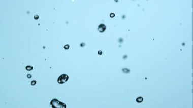 Kristal berrak su damlacıkları ve kabarcıkları havada açık mavi bir zemine karşı çok yavaş çekimde ve çok güzel sıvı desenlerle birlikte düşüyor.