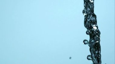 Kalın bir su akıntısı dikey olarak açık mavi bir zemine dökülüyor. Etrafında bir sürü sıçrama ve küçük damlalar uçuşuyor.