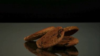 Çikolata parçacıklı ve yulaf ezmesi gibi farklı türde kurabiyeler siyah arka planda karanlık bir yansıtıcı yüzeyde birikir ve birikir.