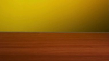 Tek bir çikolatalı kurabiye havadan düşüyor ve parlak sarı arka plan yüzeyine karşı parlak ahşap bir masada zıplıyor.