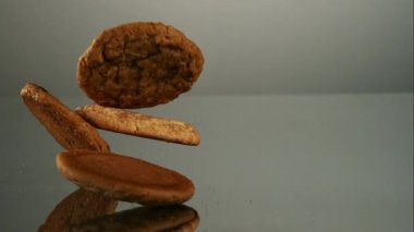 Düşen ve zıplayan çeşitli tatlardan oluşan birden fazla kurabiye kırıntıları ve uçuşan şeker tozu ile yavaş çekimde gri yansıtıcı bir yüzey üzerinde